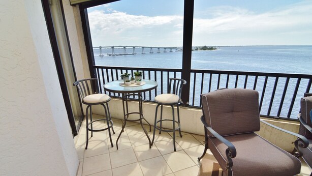 Ein Balkon mit Tisch, zwei Stühlen und Blick auf eine Brücke über dem Wasser.