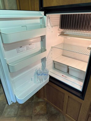 Avoin jääkaappi, jossa on useita hyllyjä ja pakastelokero.