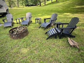 A grassy outdoor area with several Adirondack chairs and a metal fire pit.