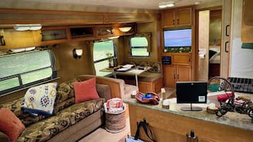 A cozy RV interior with a sofa, a small table, a TV, and a kitchenette area.