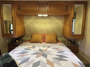 A bedroom with a bed, two nightstands, a quilt, and wooden cabinets above the bed.