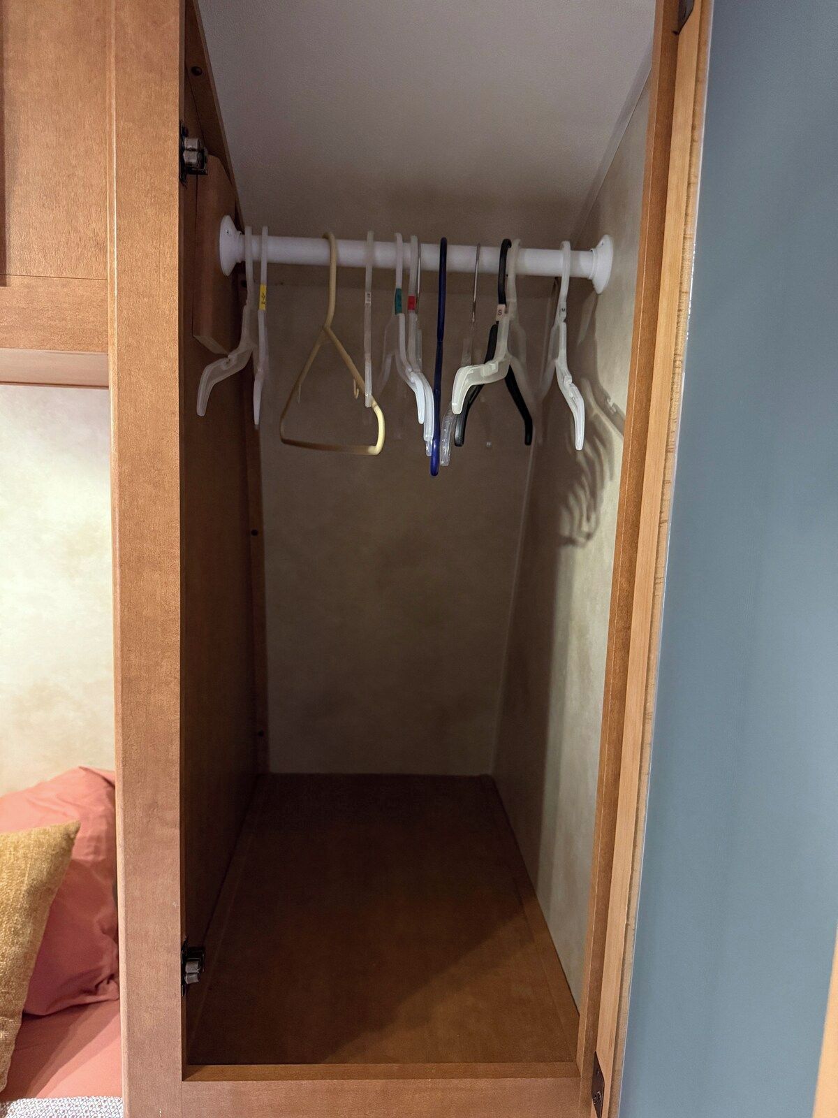 Un armadio con una porta in legno, un'asta appendiabiti bianca e un pavimento marrone.