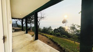 A covered outdoor area with a view of a landscaped garden and distant hills. - The Victoria Hill Cottage  (Digana)