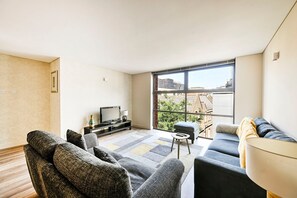 Ein modernes Wohnzimmer mit großem Fenster, einem Flachbildfernseher und einer Couch.