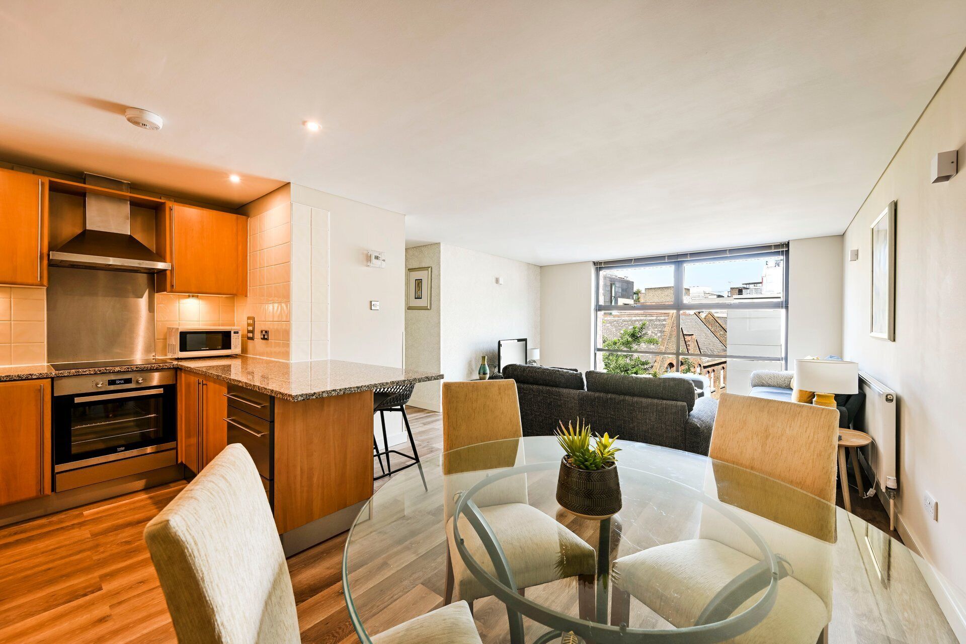 A modern kitchen with stainless steel appliances, a glass dining table, and a view of the city through large windows.