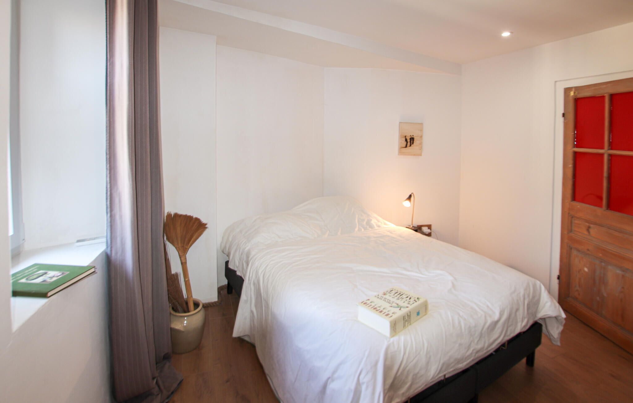 A bedroom with a bed, a bedside lamp, a window with a view, and a door with a red panel.