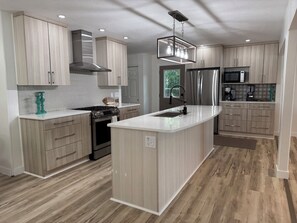 A modern kitchen with a central island, stainless steel appliances, and light wood cabinetry.