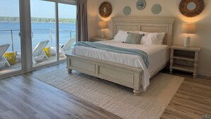 Quarto com uma cama grande, vista para a água e varanda com cadeiras.