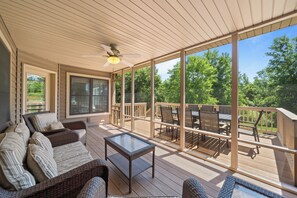 A covered outdoor deck with wicker furniture, a glass table, and a ceiling fan. - Geneva Haven: A Family Retreat I Game Room + Outdoor Entertaining I Accessible (Lake Geneva)