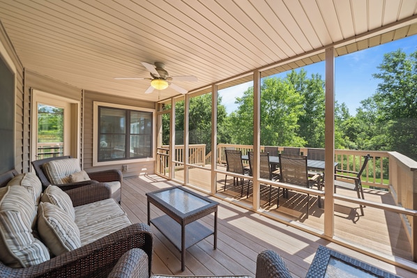 A covered outdoor deck with wicker furniture, a glass table, and a ceiling fan.