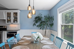 A dining area with a wooden table, blue chairs, a vase with flowers, and hanging pendant lights.