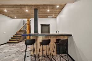 Une cuisine avec un îlot central en bois, des tabourets de bar, un escalier et une porte.