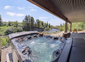 A hot tub with a river view, outdoor seating, and a covered area. - Luxury Riverfront 5BR Lodge with hot tub, fireplace, custom bar, and mountain views. (Ashton)