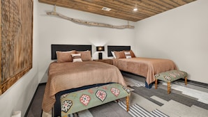 Ein Schlafzimmer mit zwei Betten, einer Holzbalkendecke, einem an der Wand hängenden Kunstwerk und einem gemusterten Teppich.