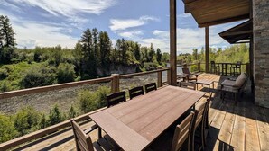 Eine Holzterrasse mit Tisch und Stühlen mit Blick auf einen Fluss und einen Wald.