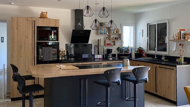 Una cocina moderna con una isla central, taburetes de bar, iluminación colgante y armarios de madera.