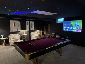 A pool table with balls, a sofa, a lamp, and a screen displaying a sports channel.