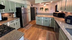 Une cuisine avec des meubles de couleur vert clair, des appareils en acier inoxydable, un plan de travail en granit et un ventilateur de plafond.