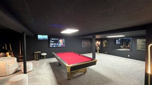 Une table de billard dans une pièce à la lumière tamisée, avec un écran de télévision diffusant un film.