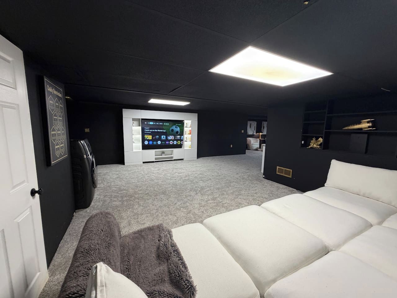 Une pièce avec un canapé blanc, un téléviseur à écran plat et un sol recouvert de moquette.