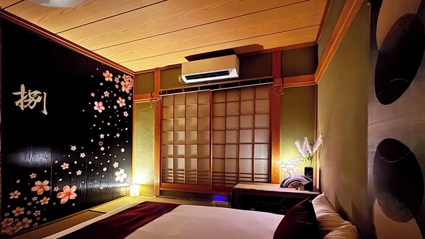 Et hotelværelse med en seng, et natbord, en væg med blomstermønster og en traditionel skydedør.