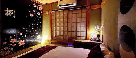 Habitación de hotel con cama, mesita de noche, pared con motivos florales y una puerta corredera tradicional.