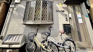 En bygning med facade af fliser, et vindue med metalgitter, en cykel og en skraldespand.