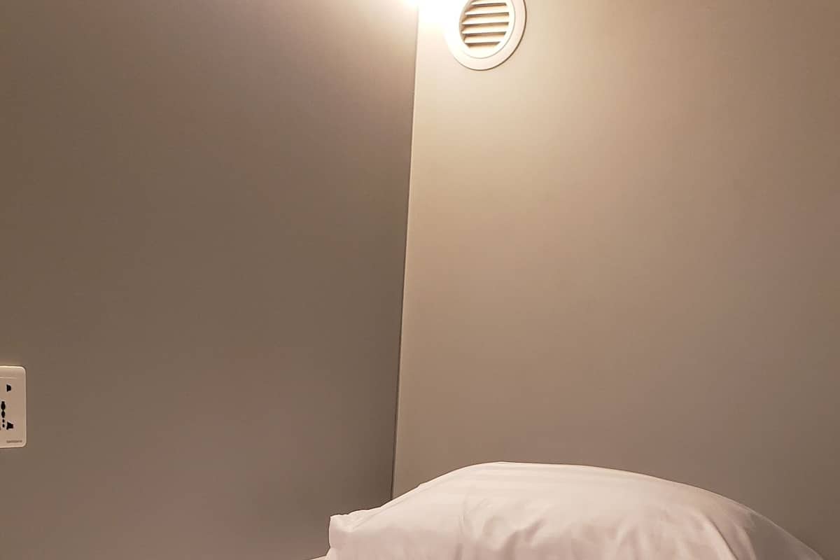 Una cama bien hecha con un almohadón blanco y un cabecero con respiradero circular.