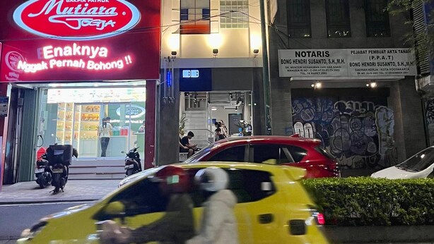 Un edificio de varios pisos con letreros iluminados que indican 'Pod' y 'Bakpia Patiok Mutiana'.
