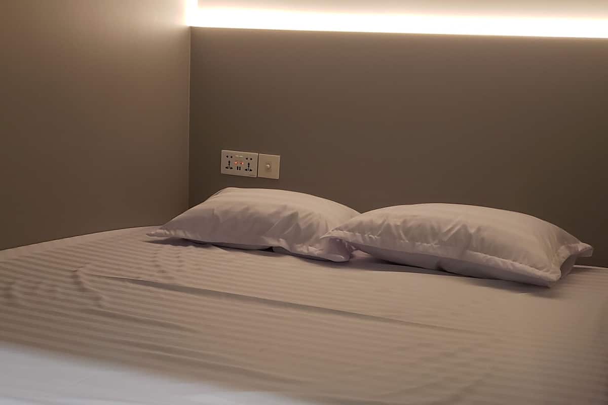 Una cama con ropa de cama blanca, un cabecero con iluminación integrada y un enchufe en la pared.