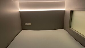 Una habitación pequeña y tenue con una cama individual, un enchufe y una ventana.