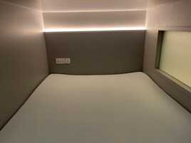 Una habitación pequeña y tenue con una cama individual, un enchufe y una ventana.