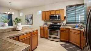 A modern kitchen with wooden cabinets, a stainless steel stove, a microwave, and a large window with blinds. - Relax, Shop & Explore from Updated Woodburn Home, Next to Outlets, Pet Friendly, Fenced Backyard (Woodburn)