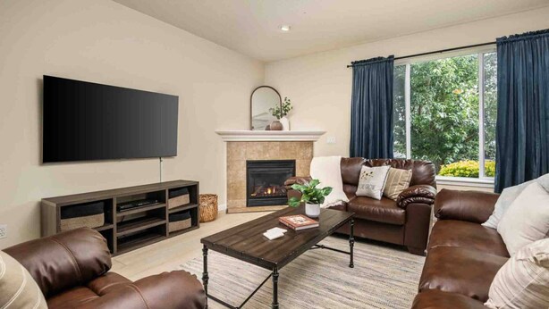 A living room with a fireplace, leather sofas, a coffee table, and a TV mounted on the wall. - Relax, Shop & Explore from Updated Woodburn Home, Next to Outlets, Pet Friendly, Fenced Backyard (Woodburn)