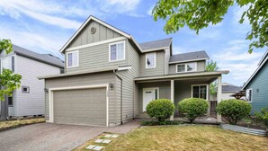 A two-story house with a garage, a front porch, and a well-maintained lawn. - Relax, Shop & Explore from Updated Woodburn Home, Next to Outlets, Pet Friendly, Fenced Backyard (Woodburn)