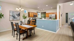 A modern kitchen with wooden cabinets, a central island, and a dining area with a wooden table and chairs. - Relax, Shop & Explore from Updated Woodburn Home, Next to Outlets, Pet Friendly, Fenced Backyard (Woodburn)