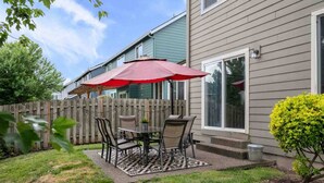 A patio with a table and chairs, a red umbrella, and a wooden fence. - Relax, Shop & Explore from Updated Woodburn Home, Next to Outlets, Pet Friendly, Fenced Backyard (Woodburn)