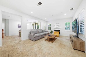Ein geräumiges Wohnzimmer mit grauem Sofa, einem Holztisch, einem Kamin und einem Fernseher.