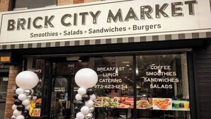 Exterior do Brick City Market, com uma placa indicando smoothies, saladas, sanduíches e hambúrgueres.