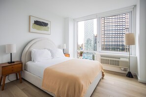 Ein modernes Schlafzimmer mit einem Bett, zwei Nachttischen, einer Stehlampe, einer Heizung und einem Fenster mit Blick auf die Stadt.