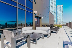Terraço no topo do prédio com área de estar ao ar livre, placa de saída de emergência e vista para a cidade.