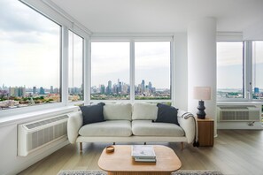 Uma sala de estar moderna com um sofá, uma mesa de centro e vista para o horizonte urbano através de amplas janelas.