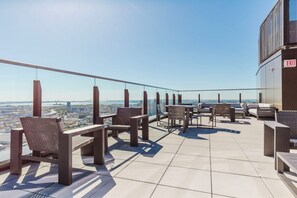 Eine Dachterrasse mit Sitzgelegenheiten im Freien, einer Glasbrüstung und Blick auf die Stadtlandschaft.