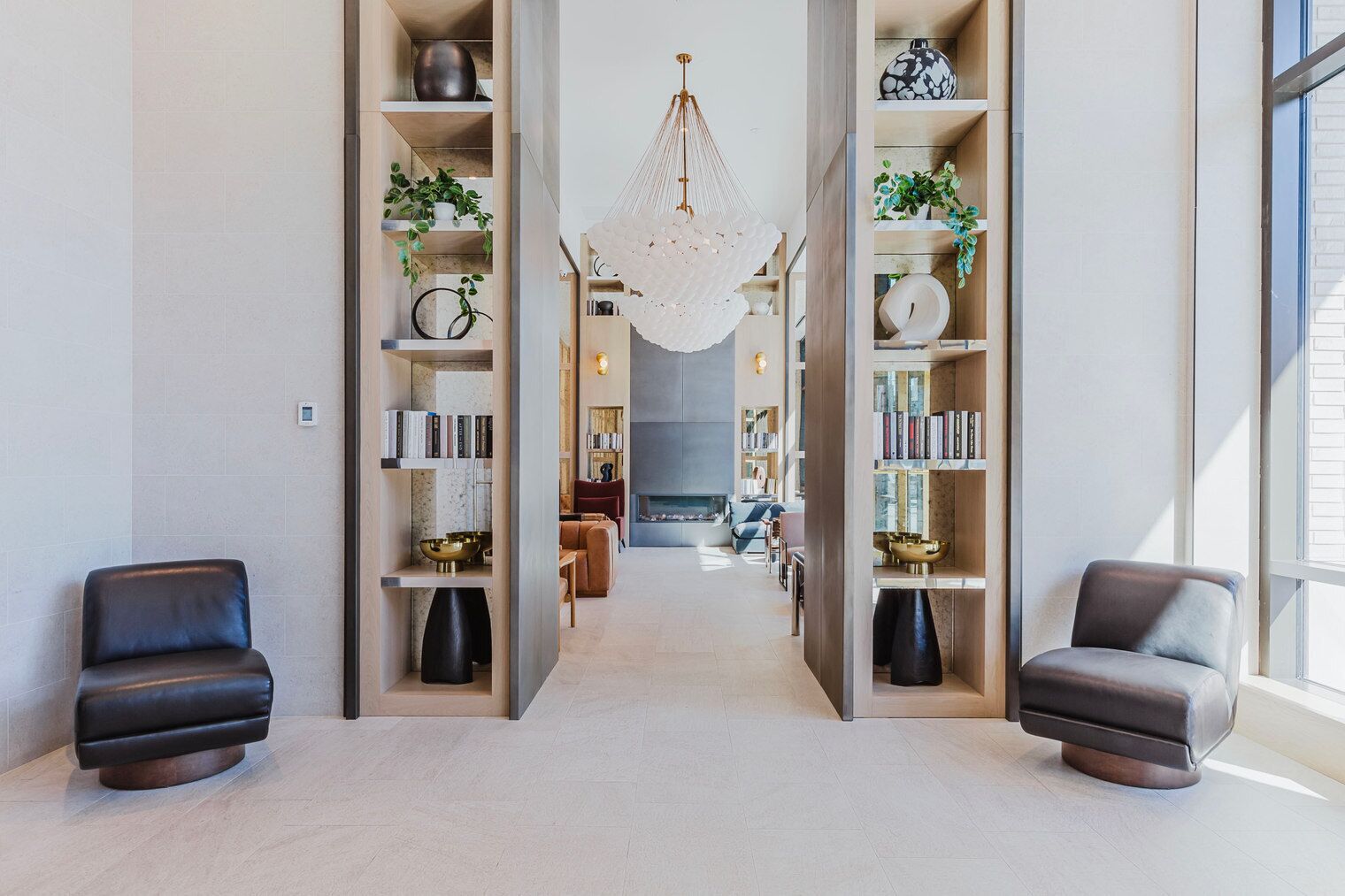 A modern living room with a fireplace, bookshelves, and two leather chairs.