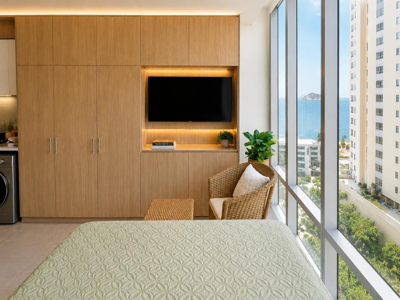 Ein modernes Schlafzimmer mit großem Bett, integriertem Fernseher, einer kleinen Sitzecke und Blick auf eine Stadtlandschaft.