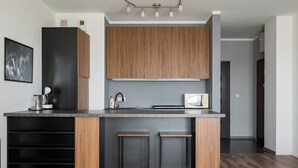 A modern kitchen with wooden cabinets, a built-in microwave, and two bar stools. - Puławska Urban Comfort Apartment (Warszawa)