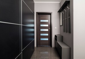 A hallway with a dark wooden door, a wall-mounted coat rack, and a small console table. - Puławska Urban Comfort Apartment (Warszawa)
