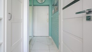 A hallway with white doors, a white door at the end, a teal wall, and a white tiled floor. - Ziemowita Colorful Studio (Warszawa)