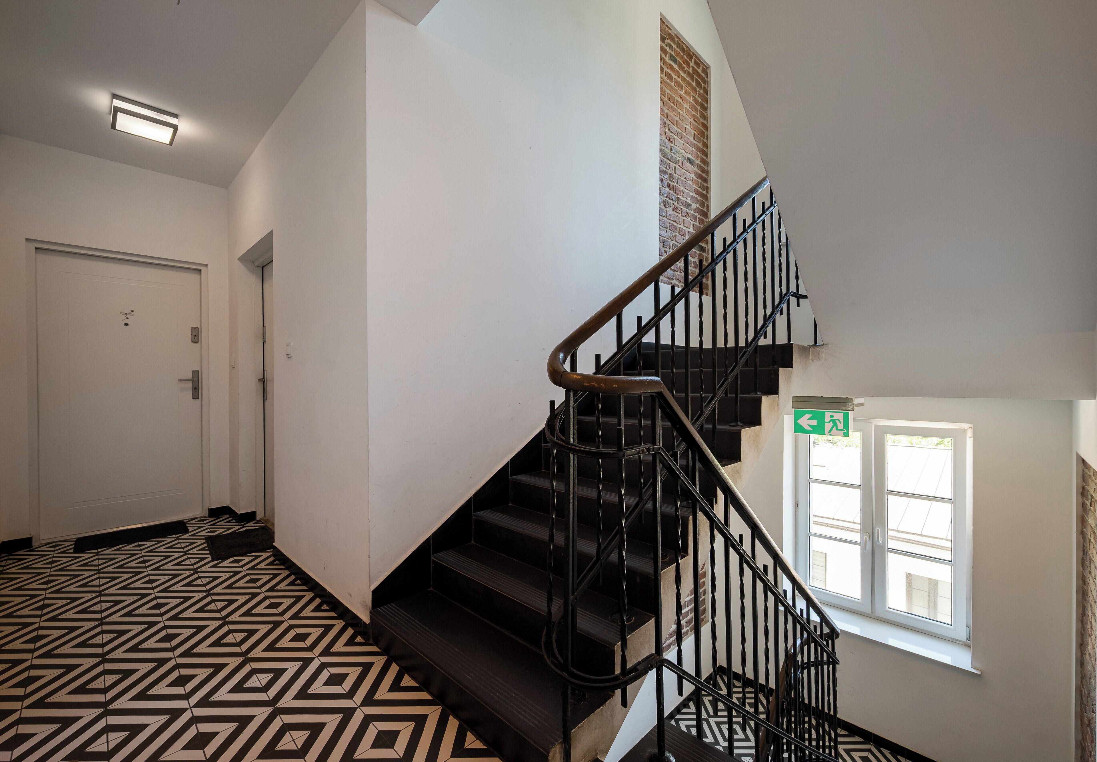 A staircase with black railings, a patterned floor, a white door, and a window with a view.
