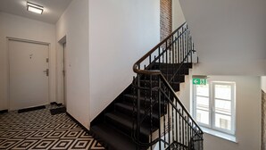 A staircase with black railings, a patterned floor, a white door, and a window with a view. - Ziemowita Colorful Studio (Warszawa)